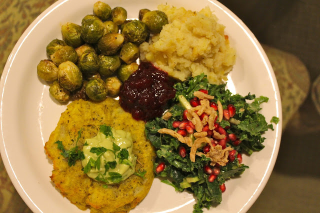 vegan thanksgiving plate of brussels sprouts, sweet potato casserole, crispy smashed potato cakes, garlic avocado aioli, shredded kale salad with pomegranate and crispy dried onions
